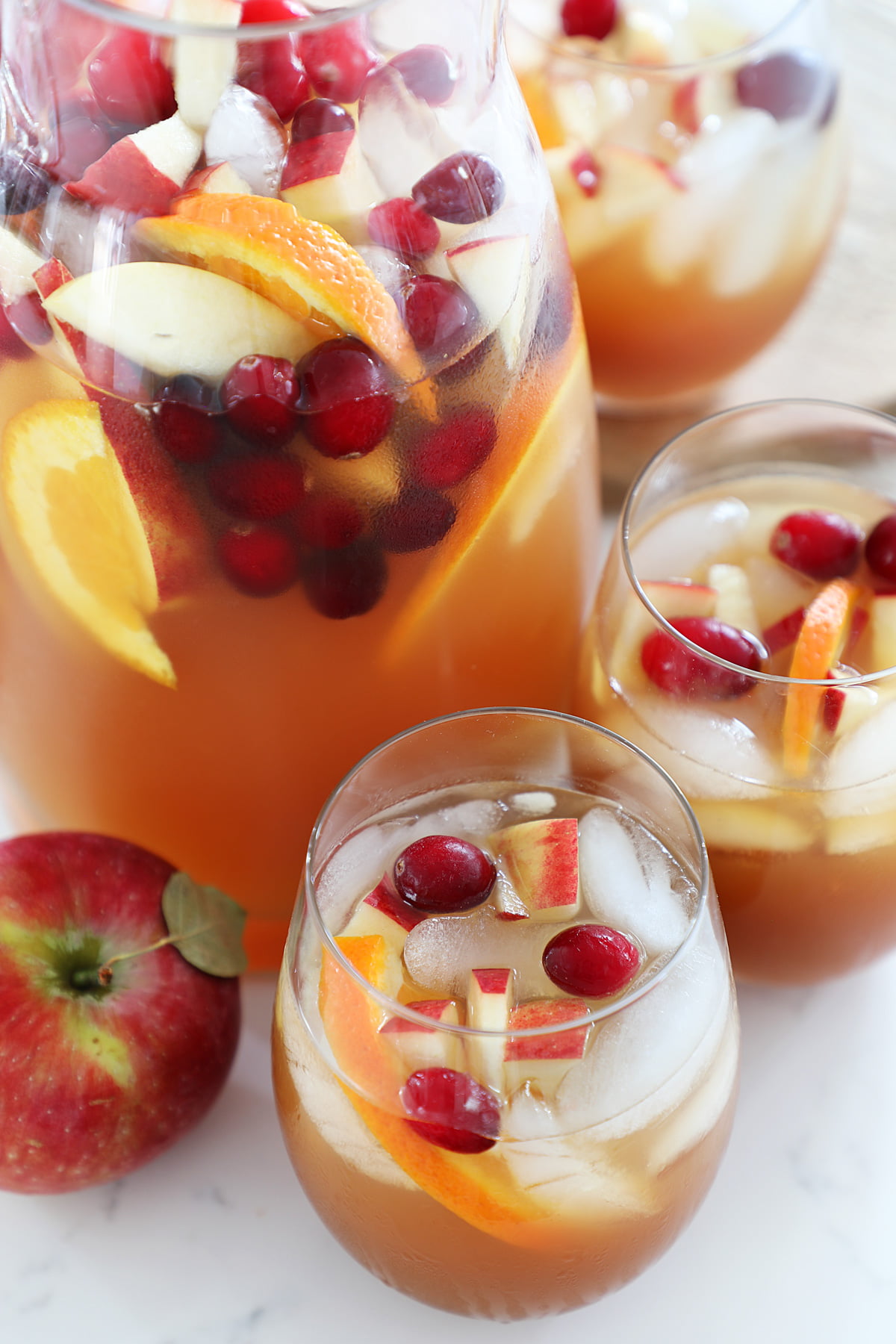 A pitcher of apple cider sangria with 3 glasses on a white counter.