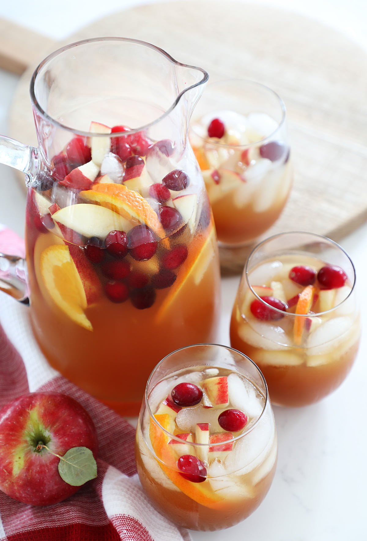 3 glasses of Apple Cider Sangria and a pitcher on a counter top with a cutting board and apples