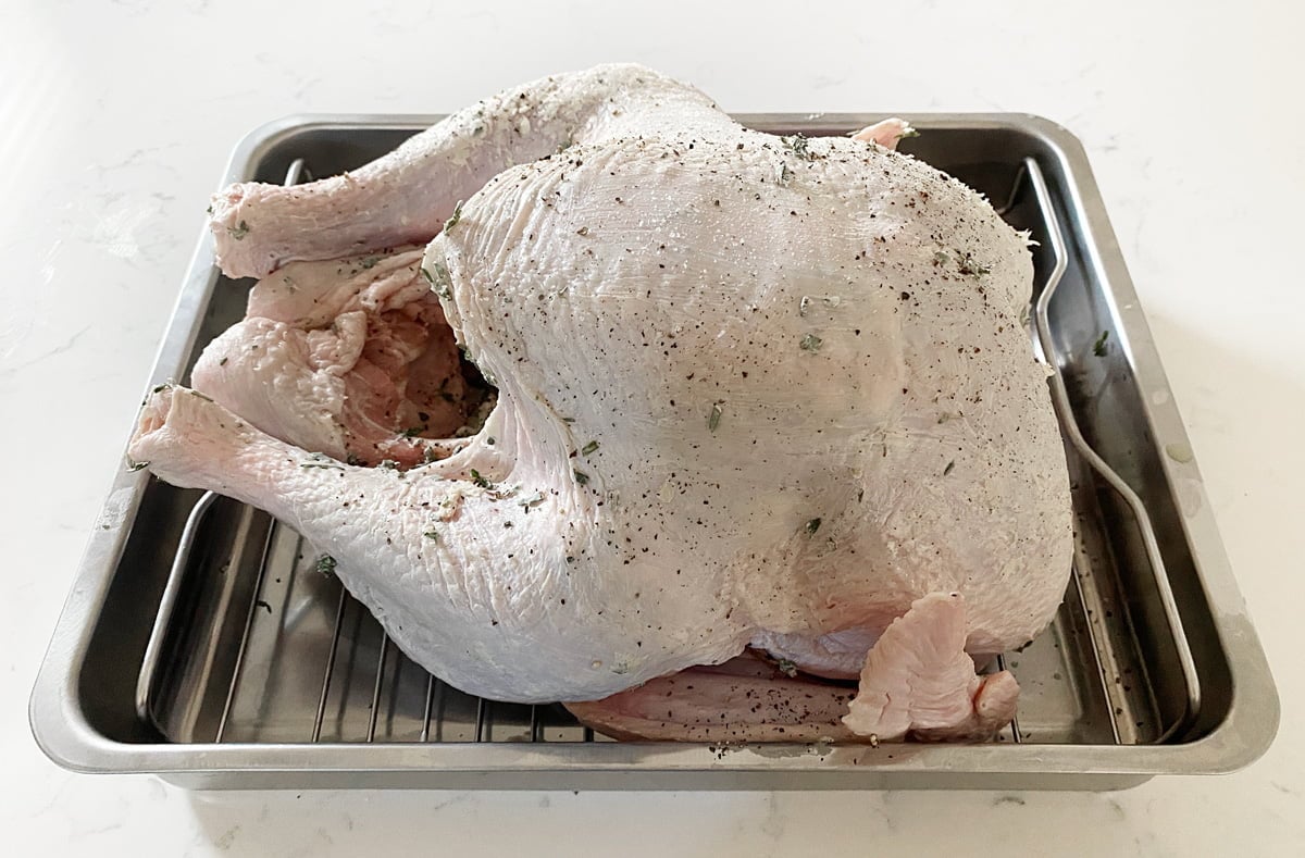 Uncooked turkey in a roaster pan with a herb butter on it. 