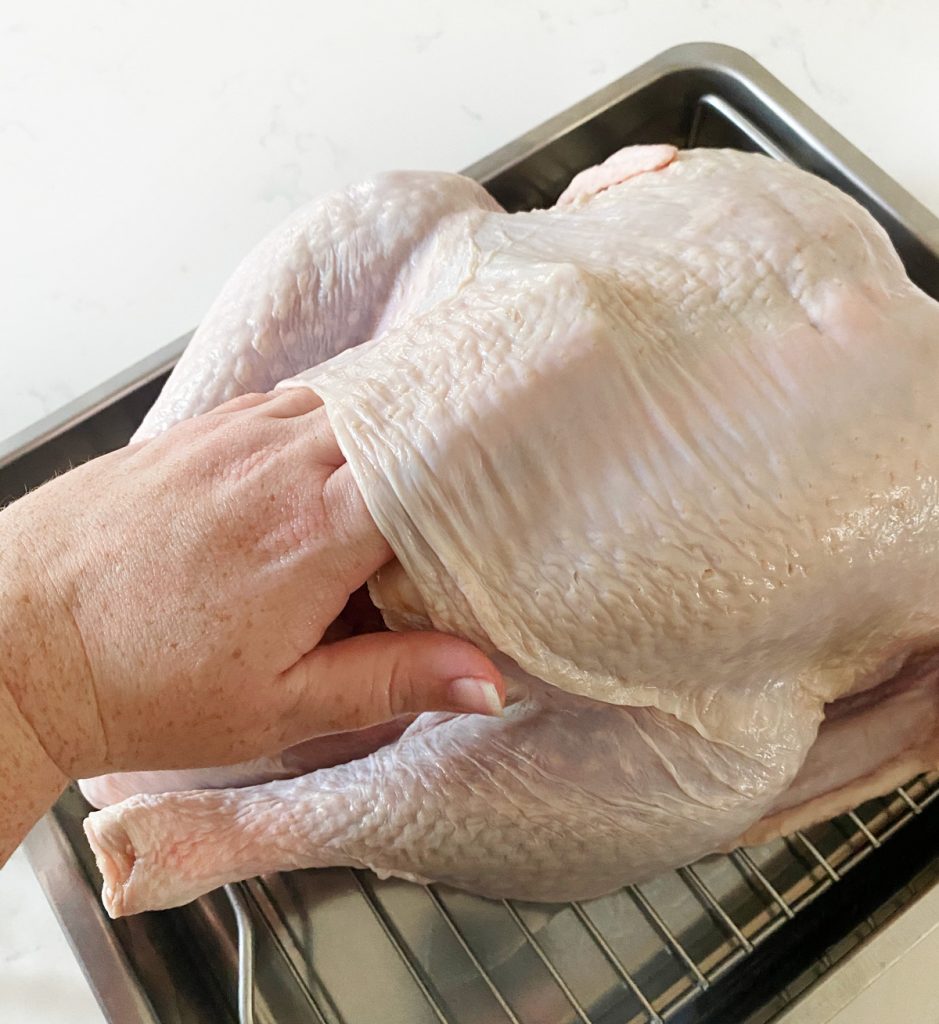 Rubbing butter under turkey skin in a roasting pan on a white counter.