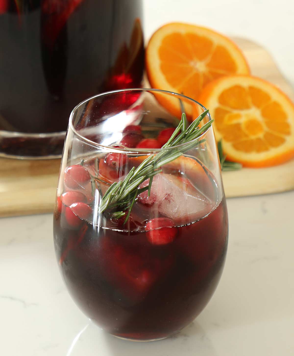 A glass of Christmas sangria on a kitchen counter with rosemary and crandberries.