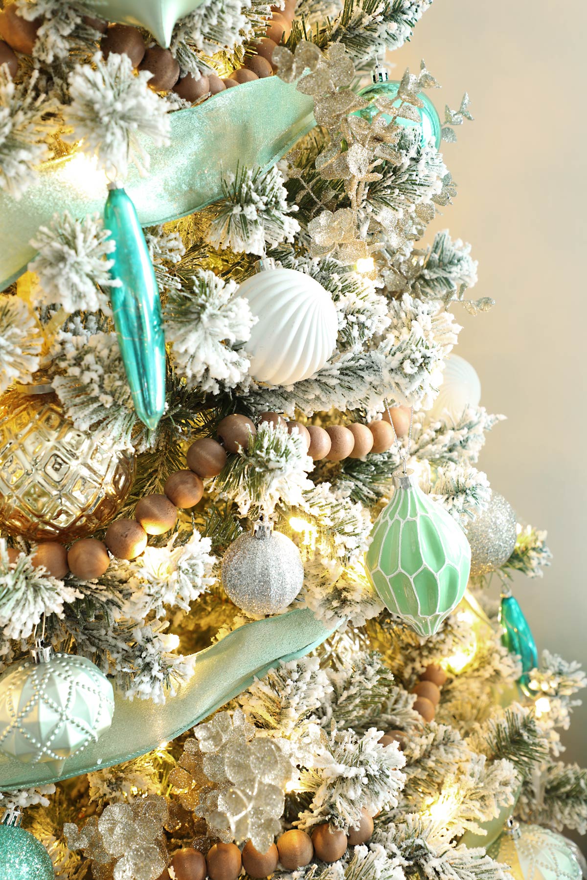 Close up of a flocked Christmas tree decorated with turquoise ornaments. 