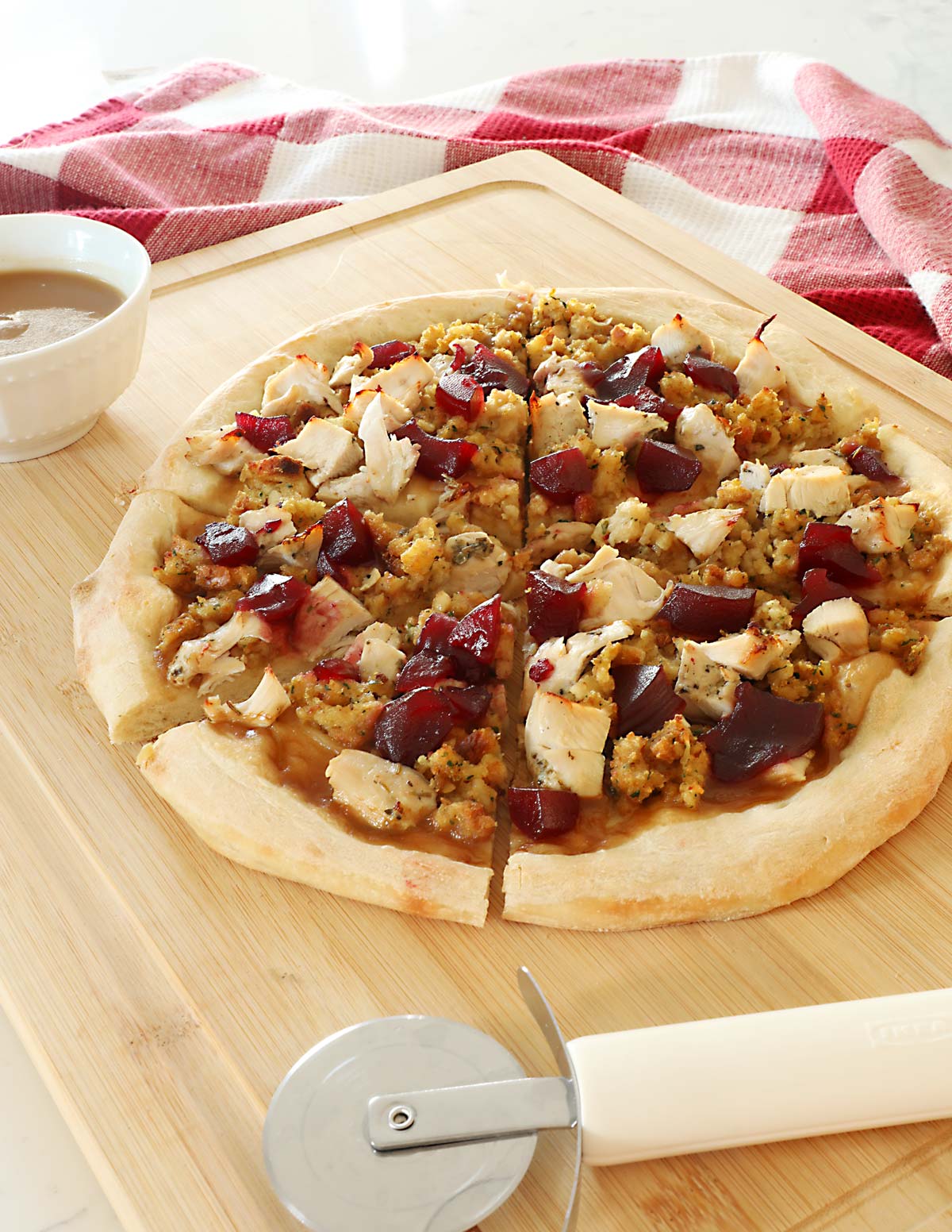 Thanksgiving Pizza on a cutting board in a kitchen with a bowl of gravy. 