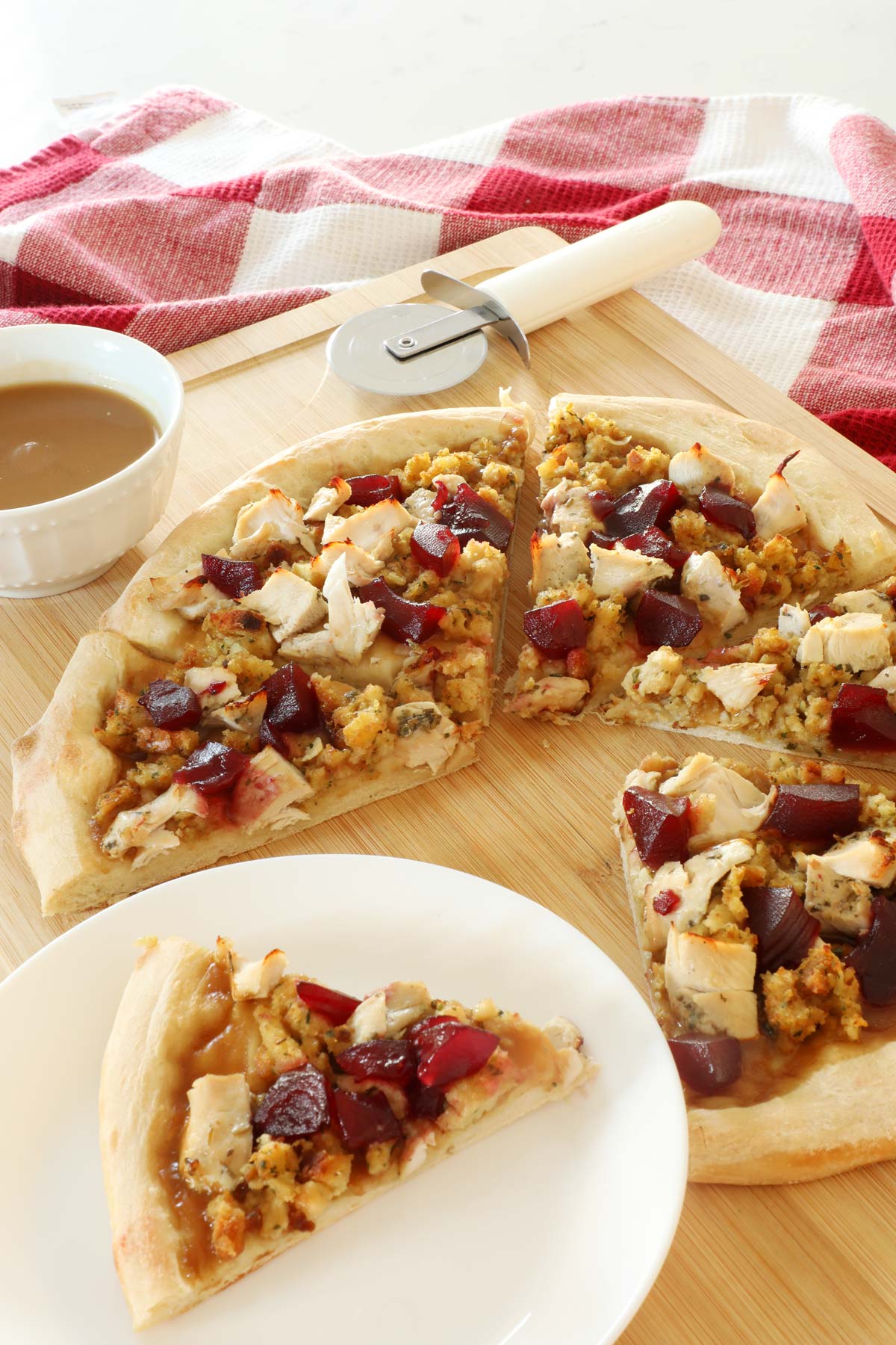 Thanksgiving Pizza on a cutting board with one slice on a white plate. 