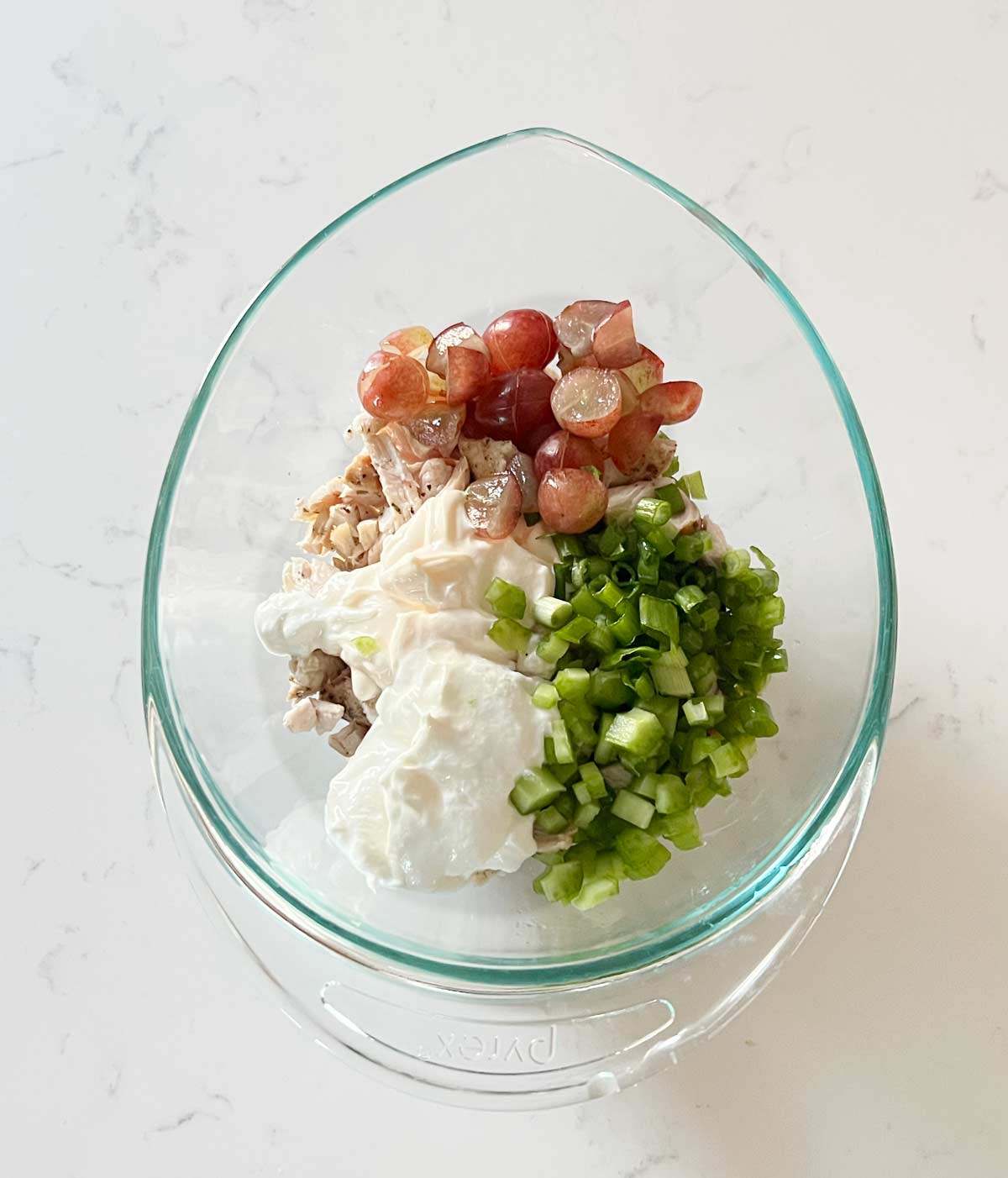 Turkey Salad ingredients in a glass bowl on a marble countertop.