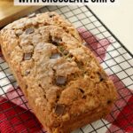 A loaf on fresh baked zucchini bread with chocolate chips cools on a cooling rack on top of the kitchen counter.