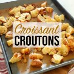 Freshly baked croissant croutons resting on a metal baking sheet on a wooden board on top of the kitchen counter.