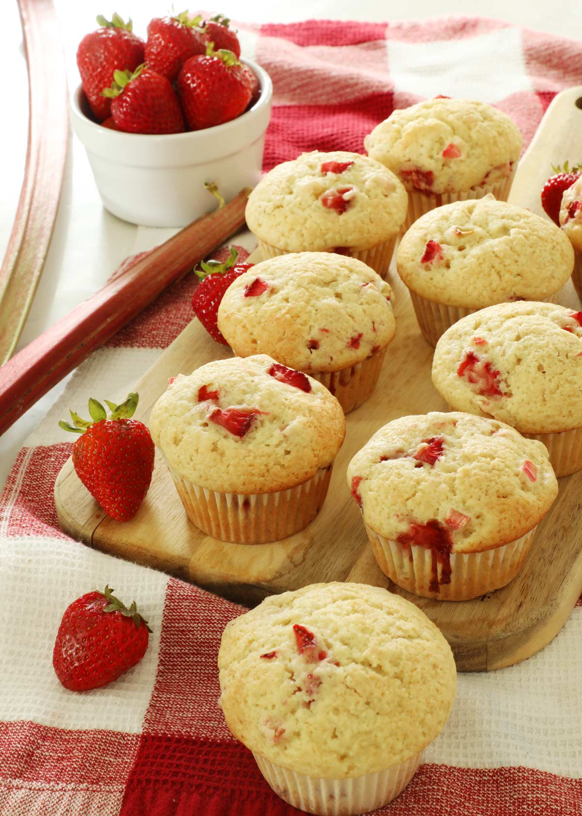 Strawberry Rhubarb Muffins on a cutting board atop a red and white kitchen towel.