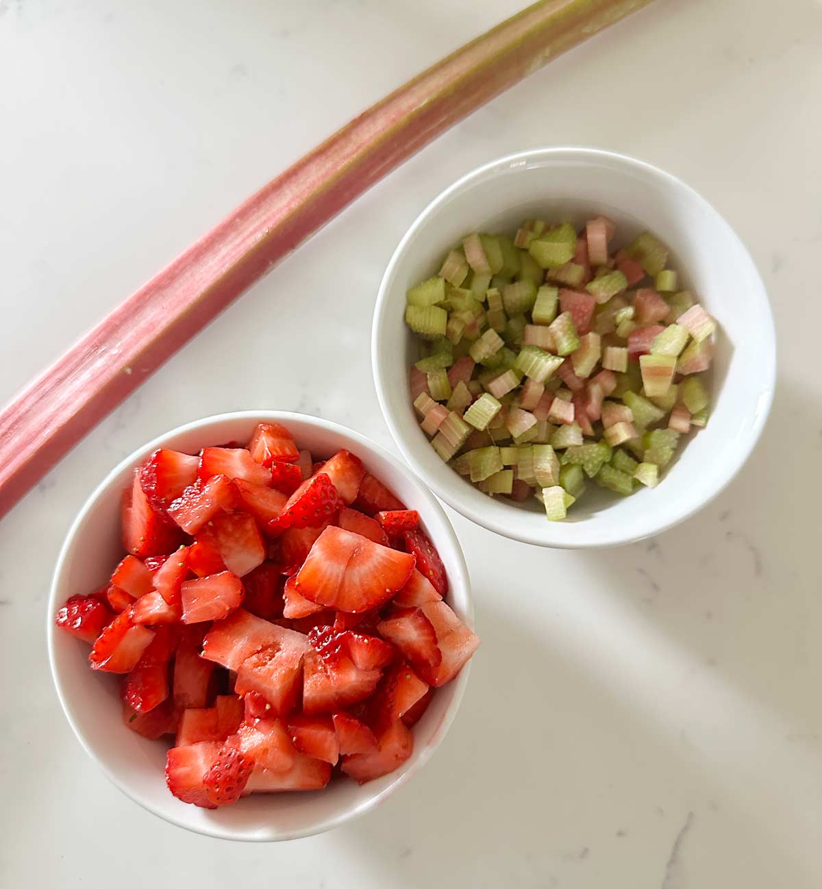 Two small bowls of strawberries and rhubarb on a white kitchen counter. 