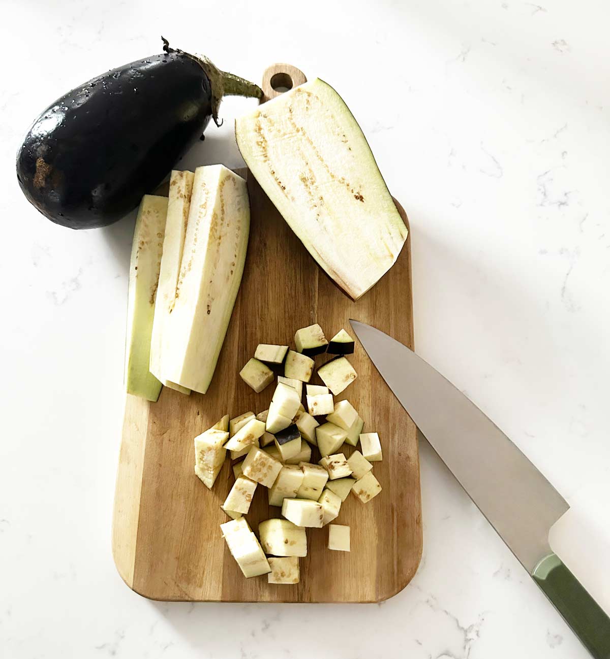 eggplant on a cutting board with a kitchen knife being diced.