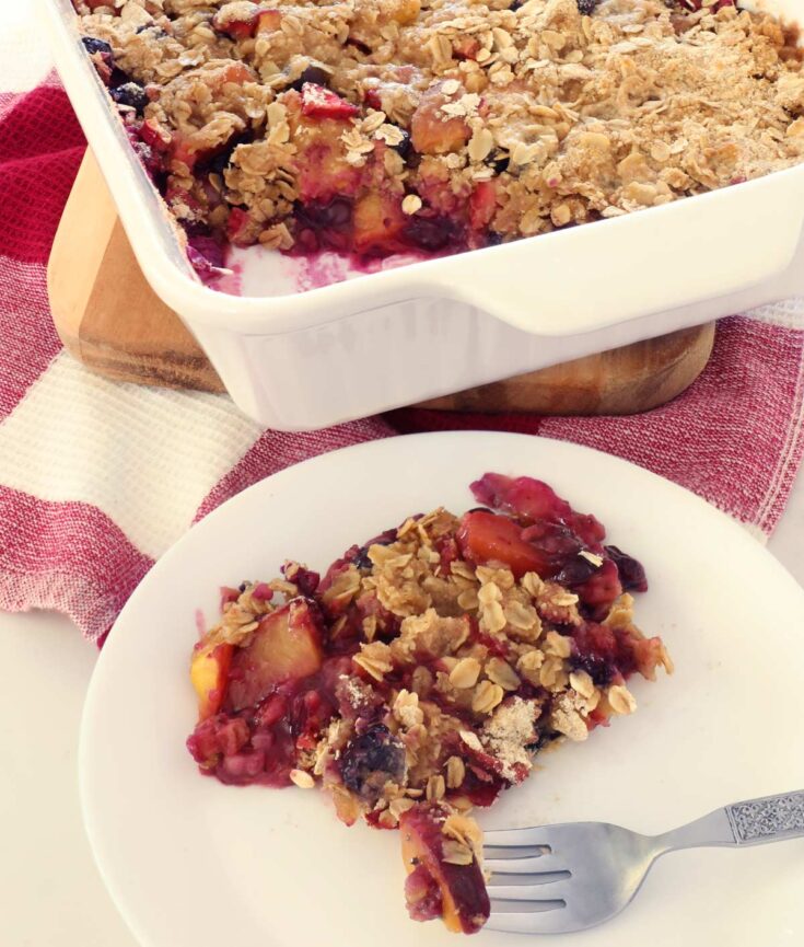 Fresh baked Fruit Crisp with peaches in a white baking dish on top of the kitchen counter.