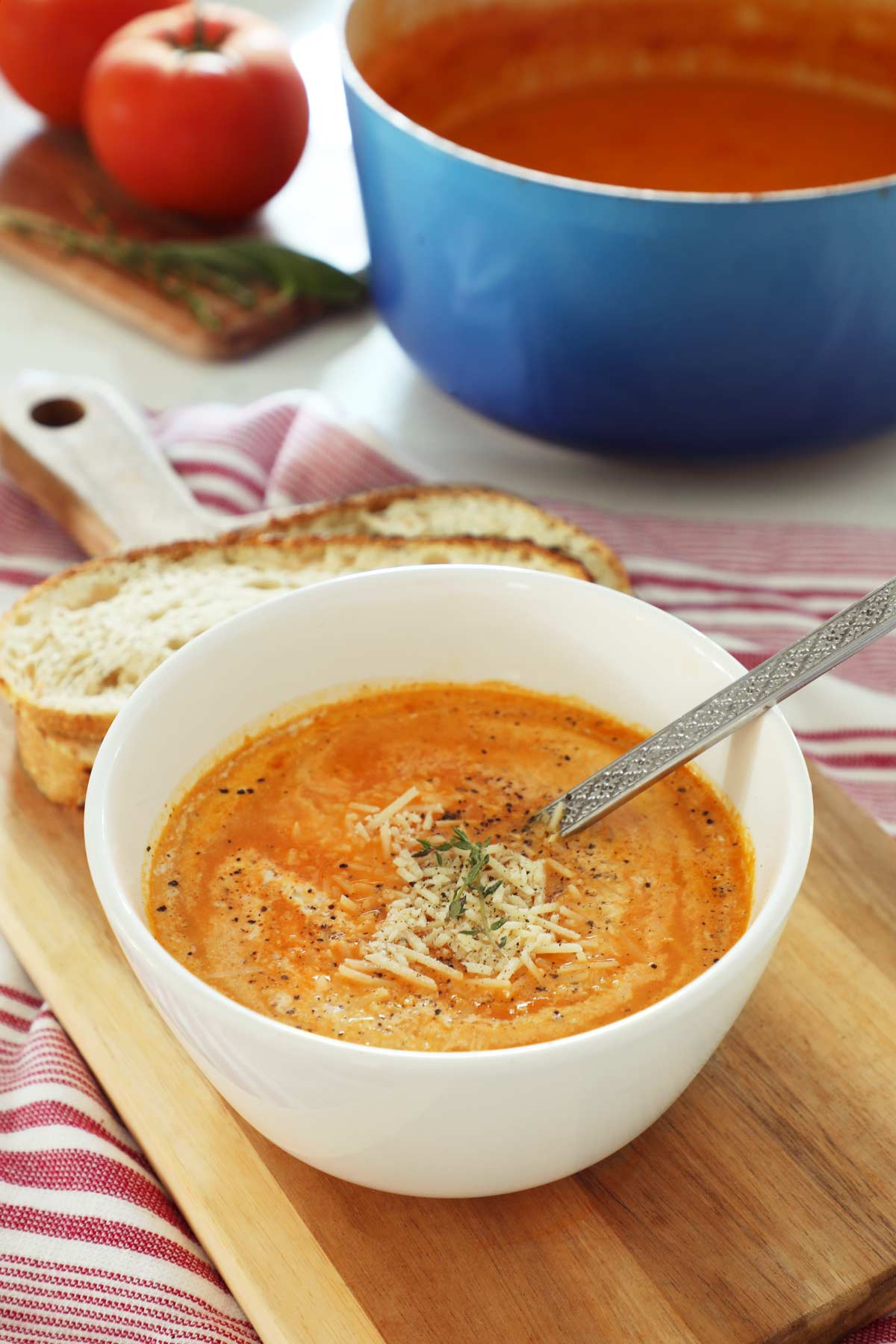 A white bowl on a cutting board filled with tomato and roasted red pepper soup.