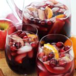 Zoomed in photo of fall sangria with ice and floating orange slices and cranberries.