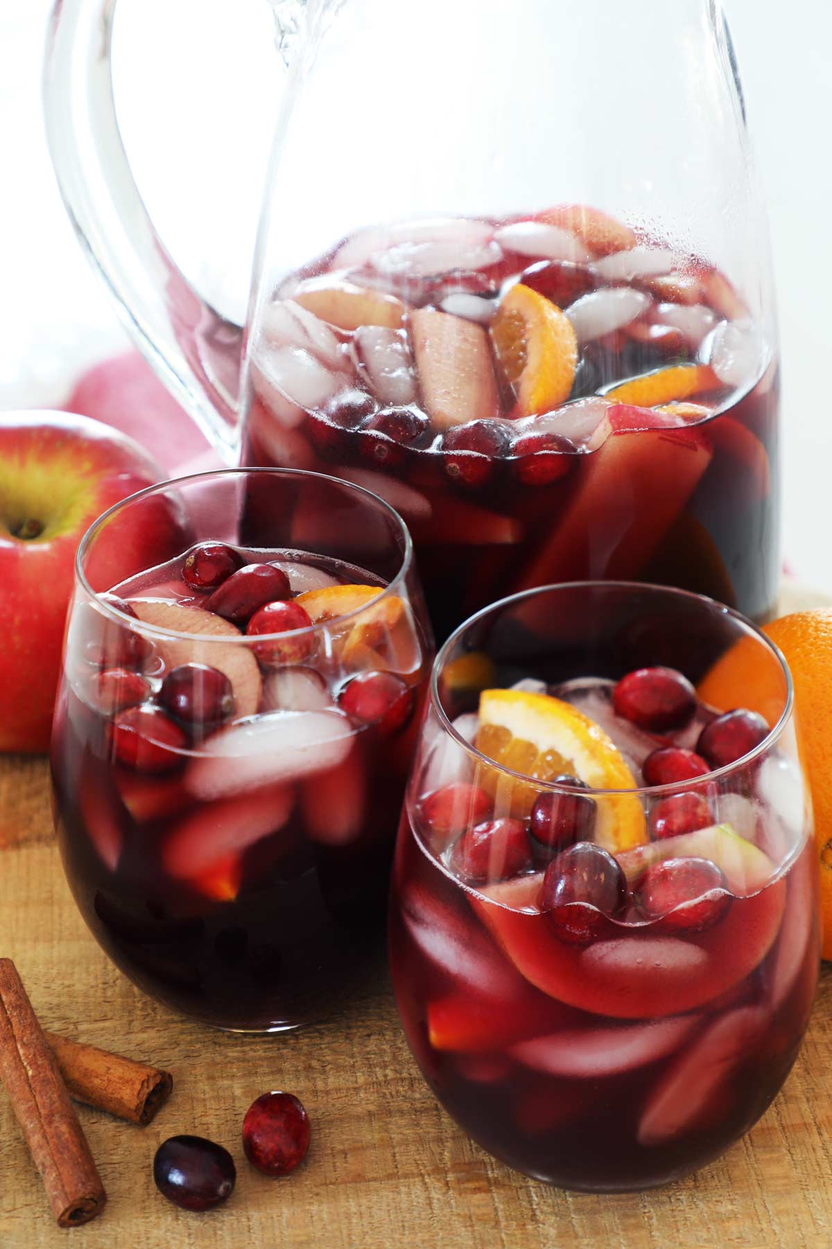 Zoomed in photo of fall sangria with ice and floating orange slices and cranberries. 