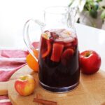 A kitchen counter with a wooden cutting board and a pitcher of fall sangria.