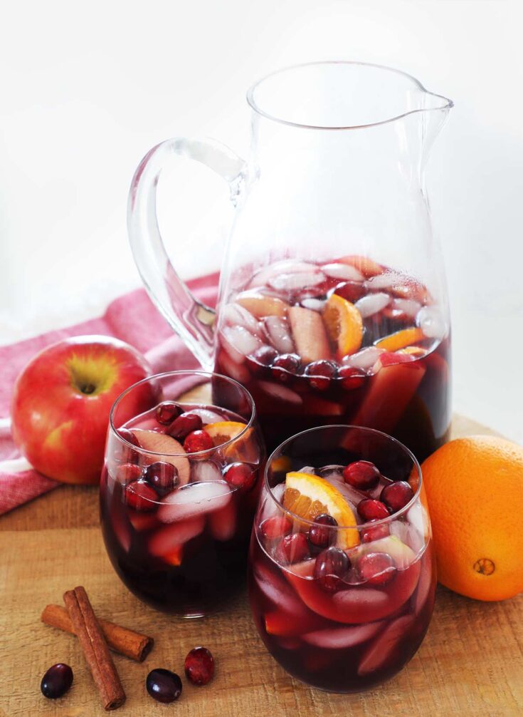 Pitcher of red apple cider sangria on a wooden cutting board with two glasses.