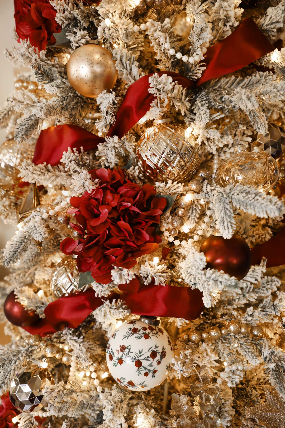Close up of an elegant flocked Christmas tree with strings of pearls, maroon ribbon, red flower accents and gold and white ornaments, Gold Star tree topper.