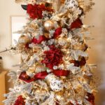 Close up of flocked Christmas tree strung with pearls, maroon ribbon, and red white and gold ornaments.
