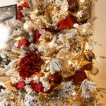 Close up of flocked Christmas tree strung with white and gold pearls, maroon ribbon, and red white and gold ornaments.