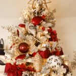 The top of an elegant Christmas tree with a golden mirror star tree topper, red white and gold ornaments, maroon ribbon and snowy bird ornament.