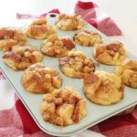 Baked french toast muffins in a light blow muffin tin on a red kitchen towel.