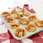 Baked french toast muffins in a light blow muffin tin on a red kitchen towel.