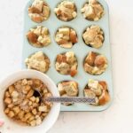 French toast muffins on a kitchen counter with a bowl of apple toppings and silver spoon.