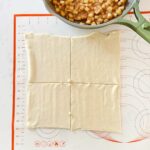 Puff pastry on a baking mat cut into squares with homemade apple filling.