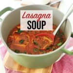 Lasagna Soup in a pot resting on wooden board and red towel on top of kitchen counter with red ladle.