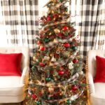 A red and green Christmas tree with plaid ribbon and ornaments with two tan wing backed chair and red pillows.