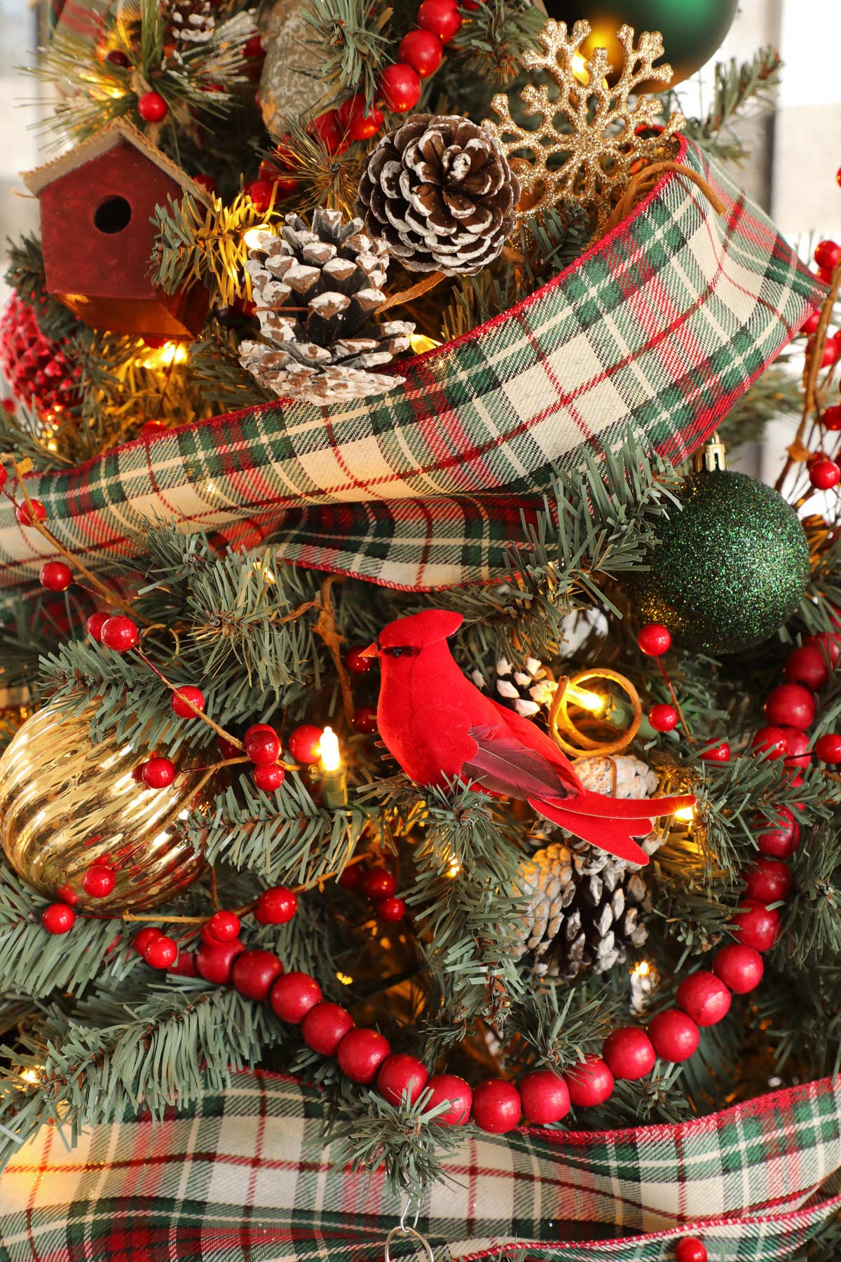 A close up of a Christmas tree with plaid ribbon, red beaded garland and a red cardinal ornament.