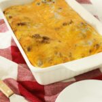 Sausage egg casserole in white casserole dish on red towel on top of kitchen counter.