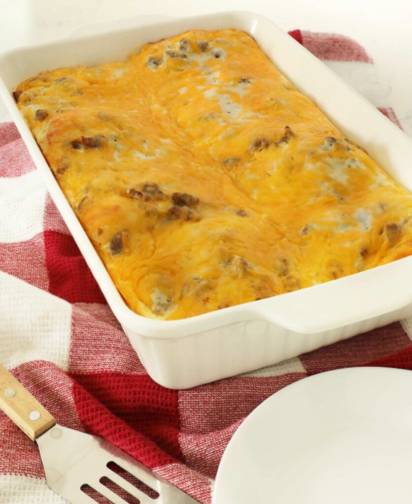 Sausage egg casserole in white casserole dish on red towel on top of kitchen counter.