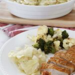 Crock pot cabbage, broccoli and cauliflower, and pork chops sit on a white plate, a large dish of crock pot cabbage sits on a wooden board in the background.