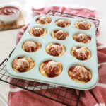 Meatball cups sitting in a teal muffin tin on the kitchen counter, marinara dipping sauce sits in a bowl off the the side.