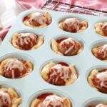 Meatball cups sitting in a teal muffin tin on the kitchen counter.