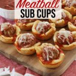 Meatball cups sit lined up neatly on a wooden board, on top of a red kitchen towel along with a bowl of marinara sauce for dipping.