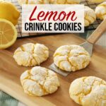 Four Lemon Crinkle Cookies sit on a wooden board, one actively being scooped up by a metal spatula while more lemon crinkle cookies cool on a rack in the background.