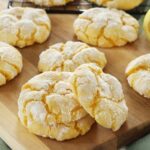 Lemon crinkle cookies sit on a wooden board and cooling rack on top of the kitchen counter.