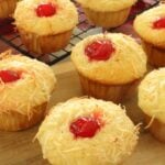 Piña colada muffin topped with a cherry on a wire cooling rack.